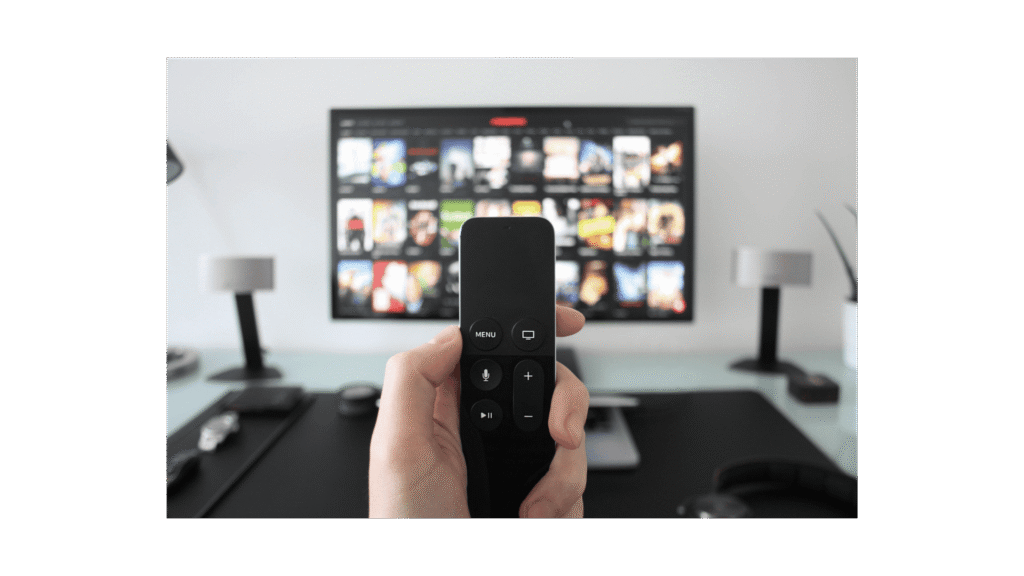 A person holding a remote control in front of a TV displaying a streaming service menu with various movie titles.