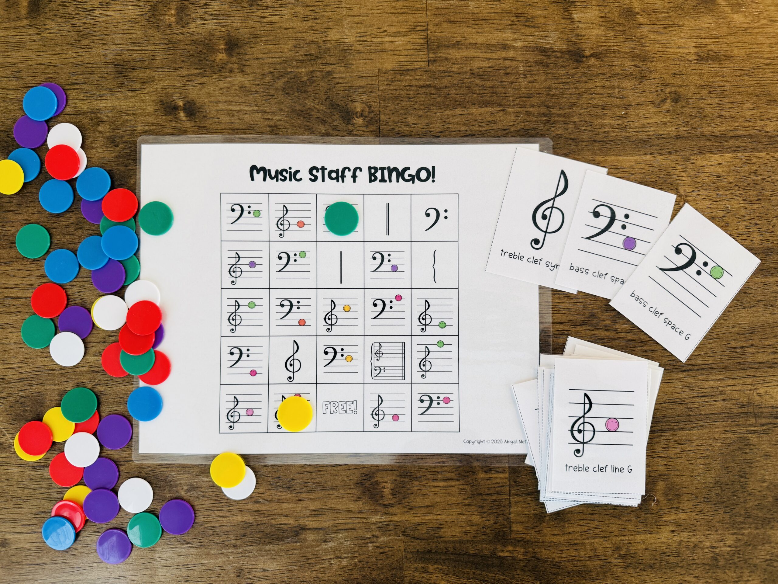 A Music Staff Bingo game setup featuring a printed bingo sheet with music notes and symbols, surrounded by colorful game tokens on a wooden table.